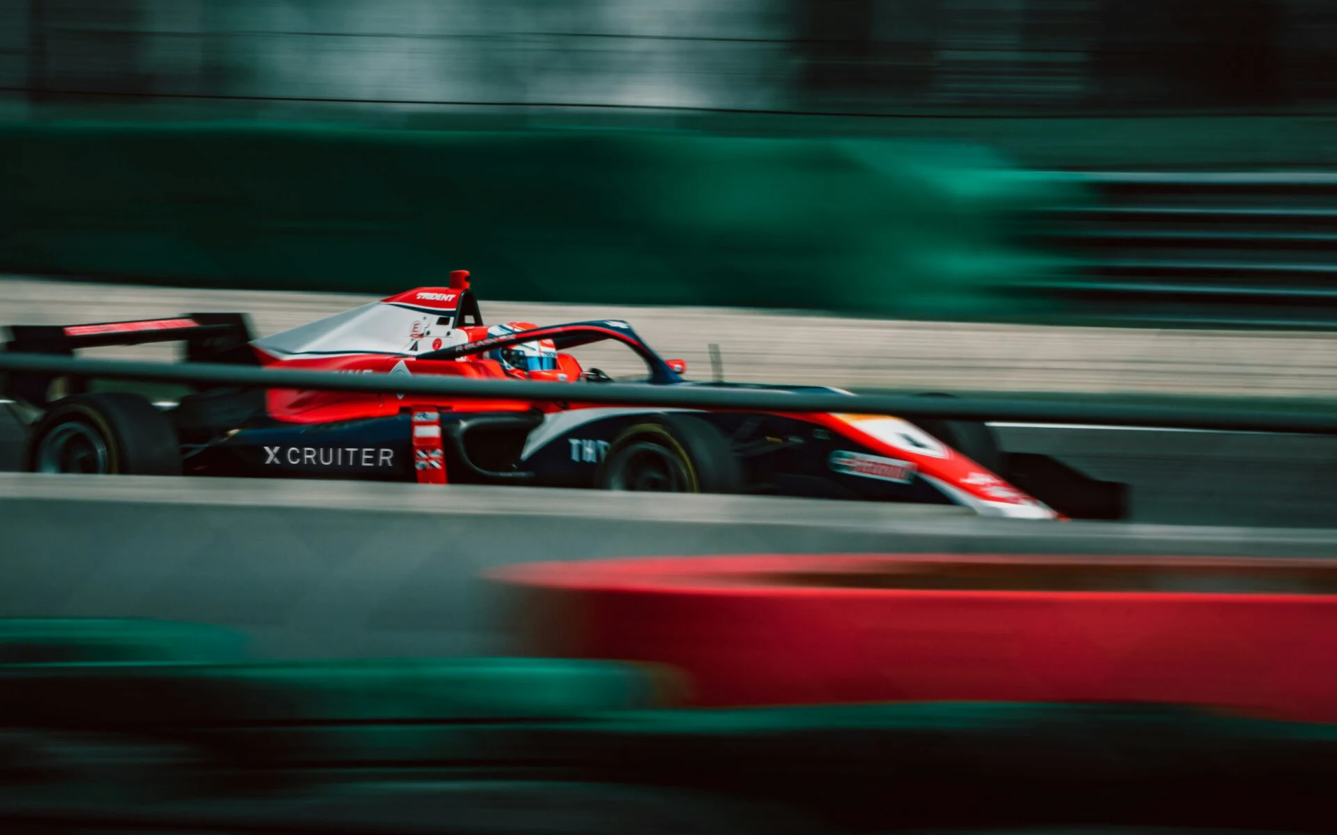 Formula 1 car bearing the Xcruiter logo, streaking past at race speed